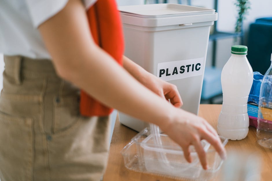 A person wearing a red shirt and beige pants is seen during a home relocation process, placing a clear plastic container with a lid next to a white plastic recycling bin labeled 'PLASTIC,' inside a ro